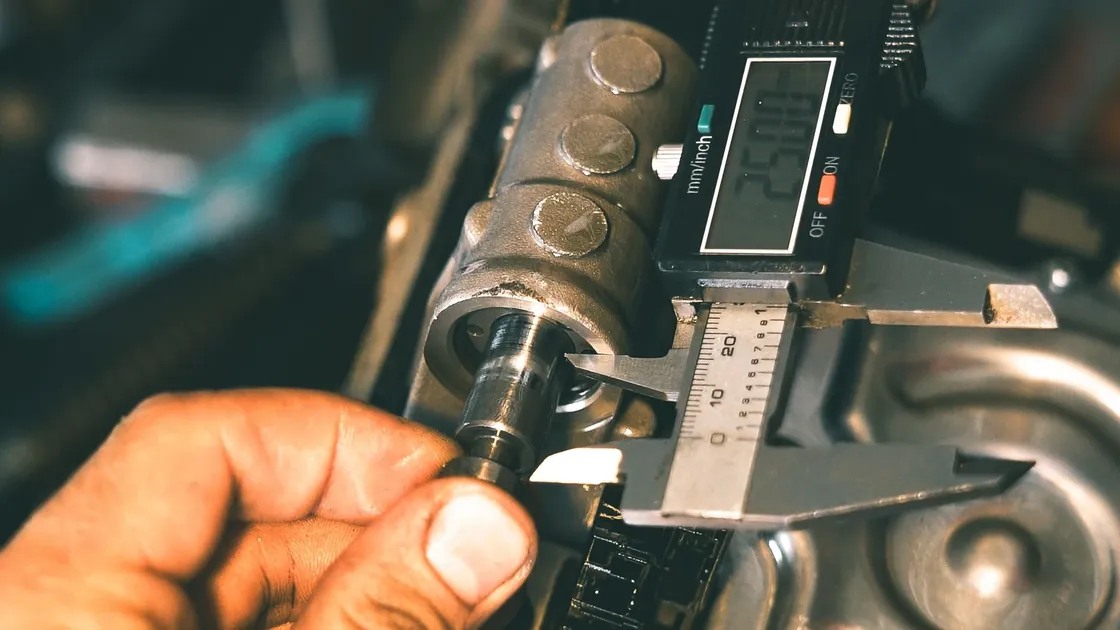 Hands measuring a machined metal component with a digital caliper.