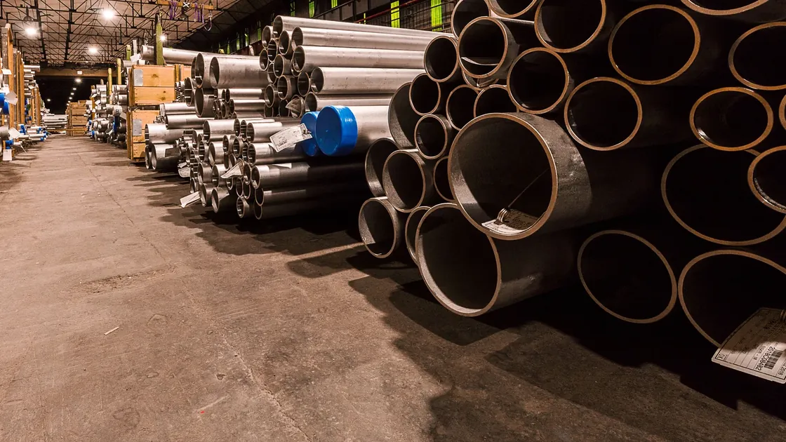Steel tubes of several diameters stored beside an industrial warehouse aisle.