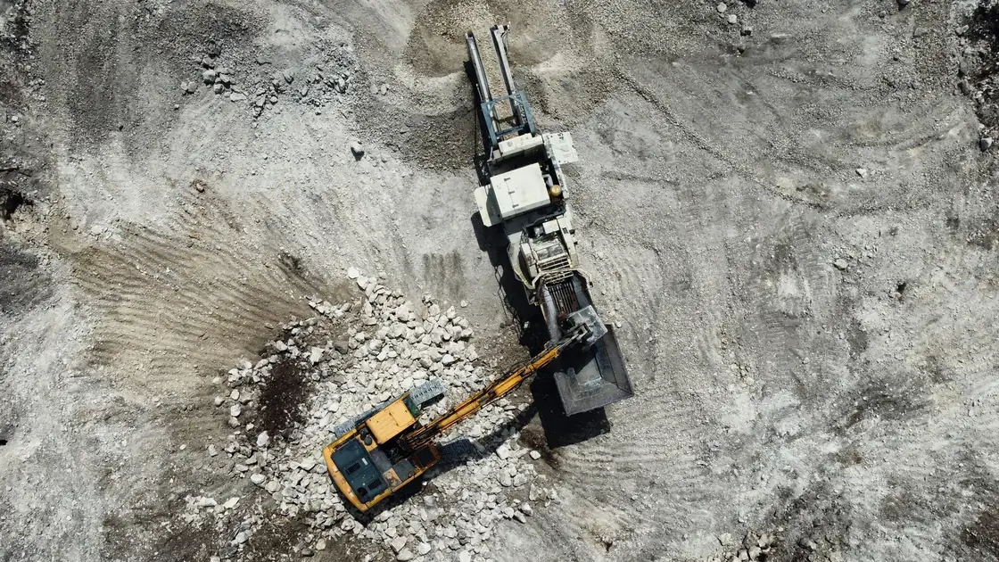 Aerial view of an excavator loading rock into a mobile crusher in a quarry.
