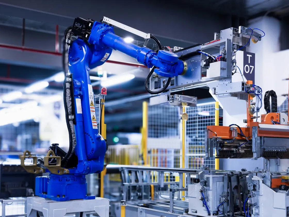 A blue industrial robot handles a refrigerator panel beside automated production equipment.